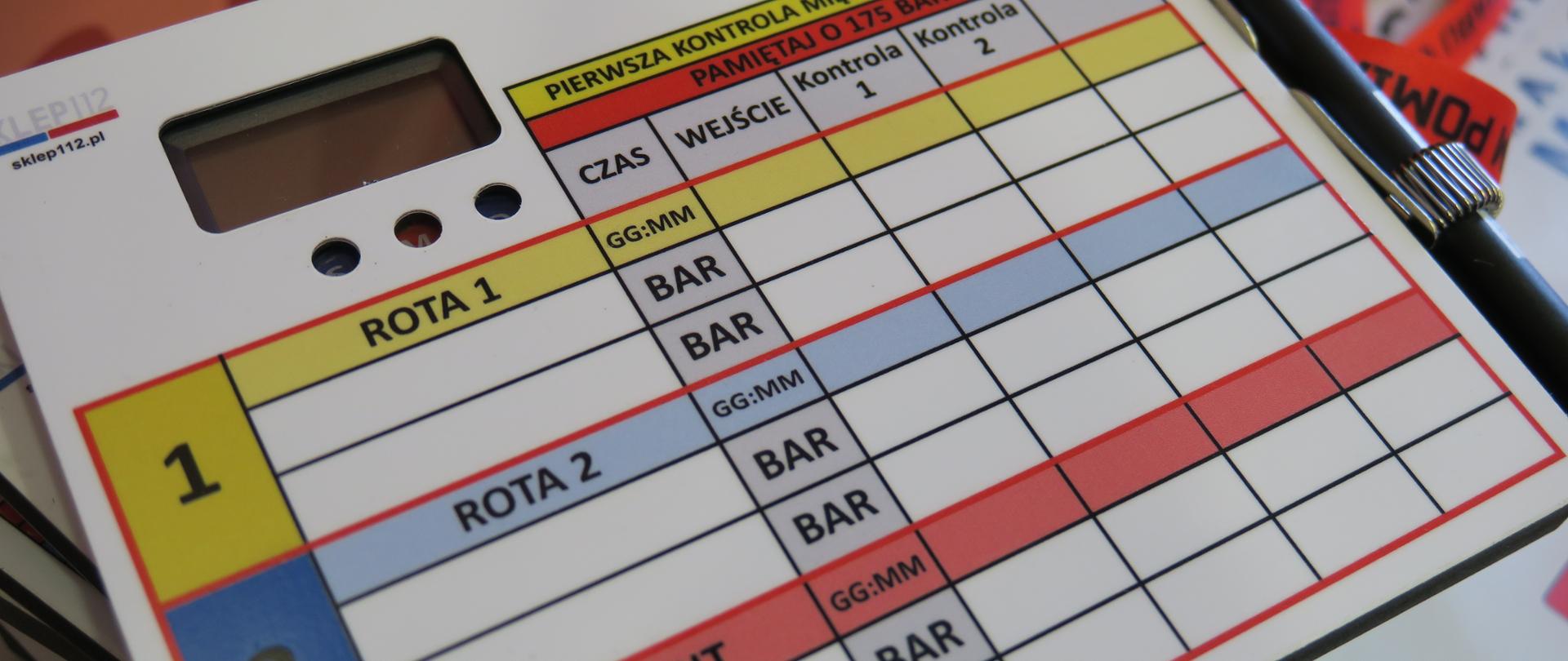 Na zdjęciu prezentowana jest tablica do pomiaru czasu pracy strażaka w strefie zadymienia. Na tablicy znajduje się tabela z podziałem na Roty, Ciśnienie w Bar czasy wejścia kontroli. Tablica posiada stoper do mierzenia czasu i długopis do zapisu parametrów koloru czarnego.