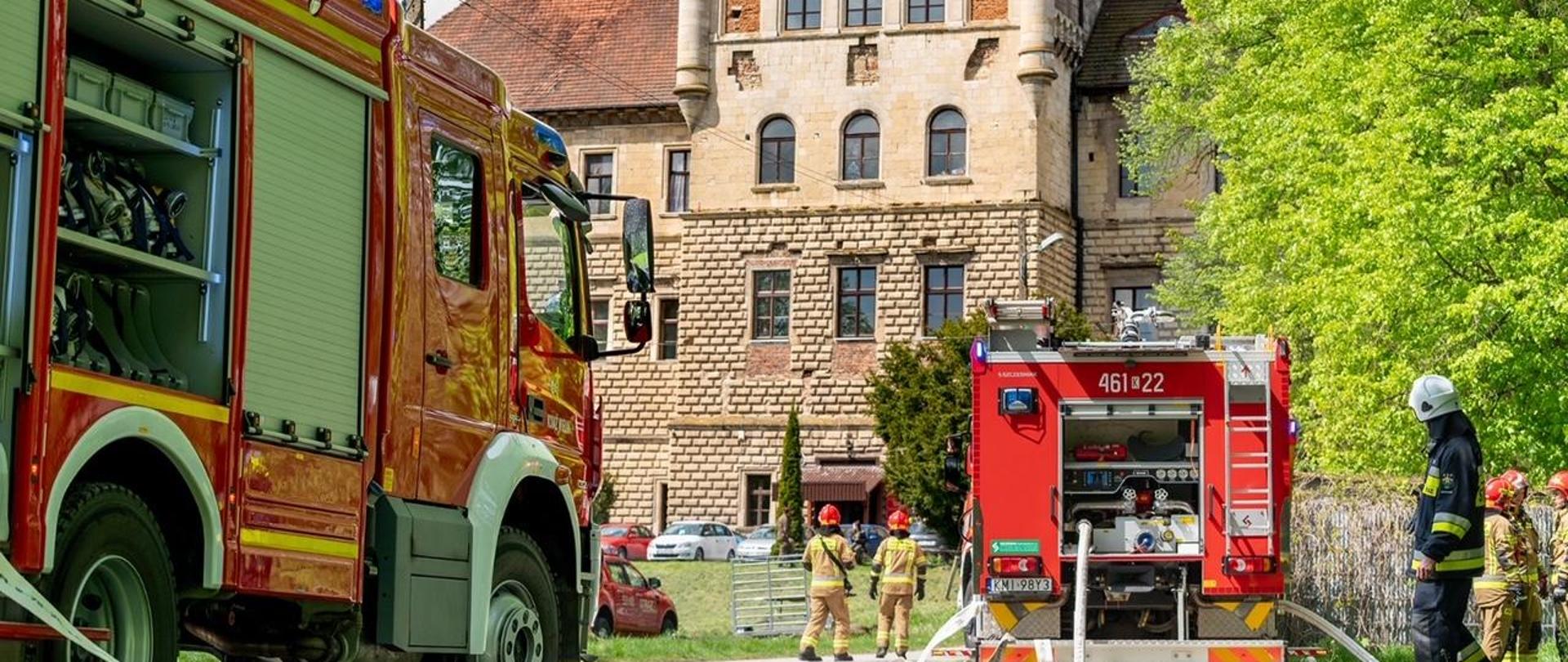 Na zdęciu wozy strażackie oraz strzały podczas gaszenia pożaru lasu na tle zamek Mirów