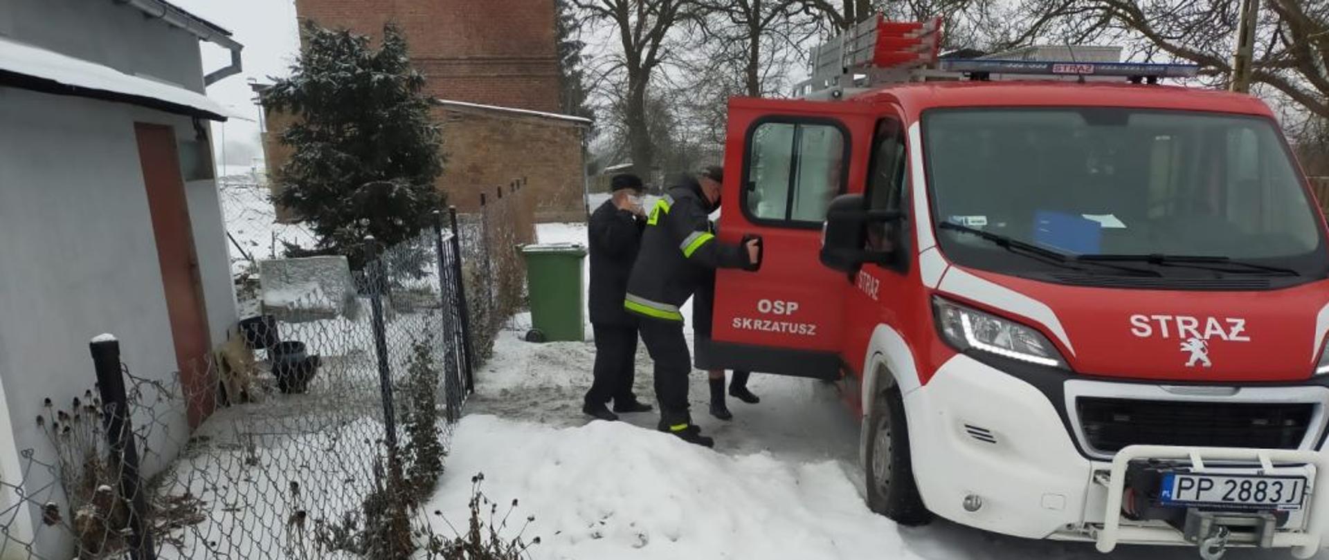Strażak pomaga wejść osobie starszej do samochodu pozarniczego celem przewiezienie na szczepienie