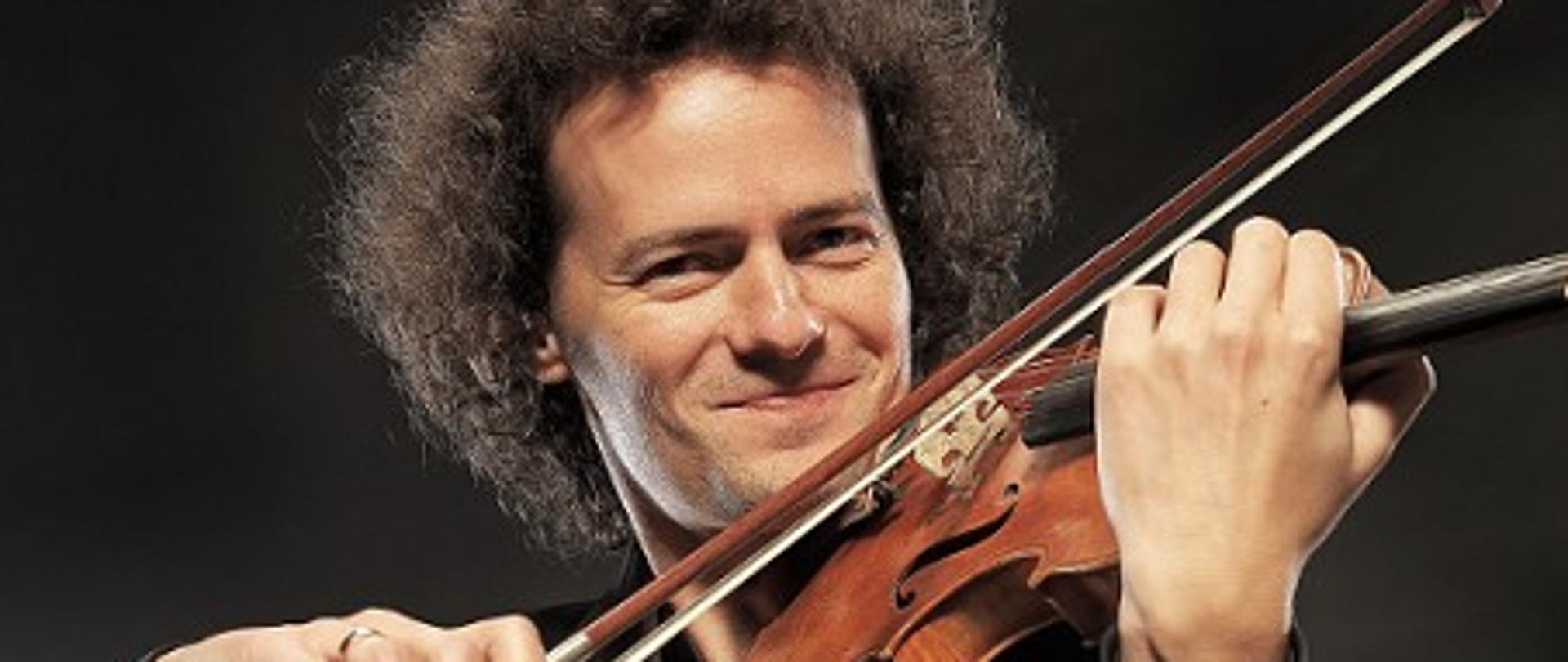 Zdjęcie przedstawia skrzypka Mariusza Patyrę we fraku grającego na skrzypcach