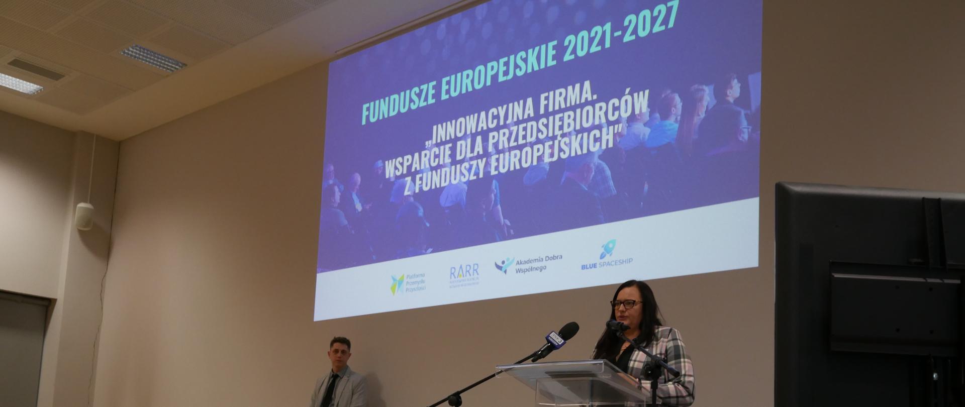 Wiceminister Małgorzata Jarosińska-Jedynak stoi na scenie przy pulpicie i mówi do mikrofonów.