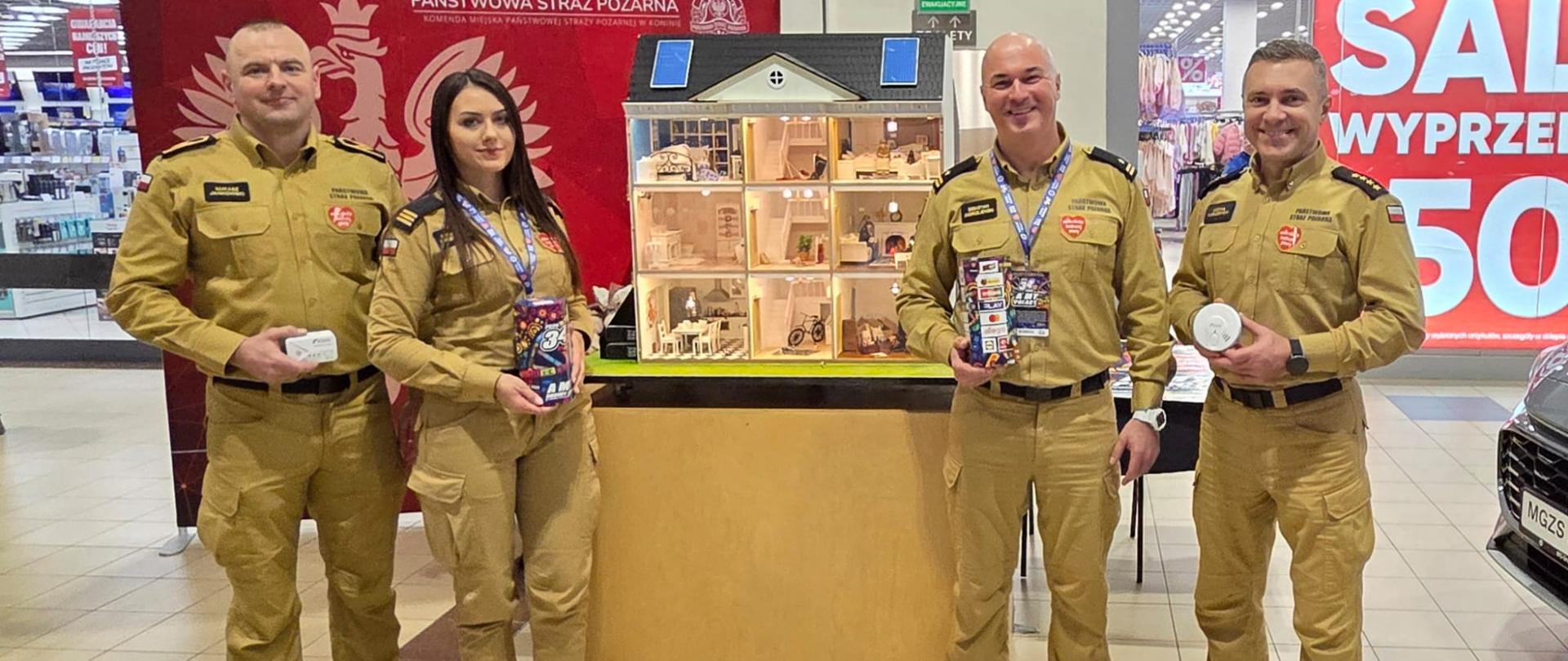 Strażacy stoją podczas finału WOŚP. Z tyłu widać mobilny symulator zagrożeń pożarowych. Strażacy ręku trzymają czujki. 