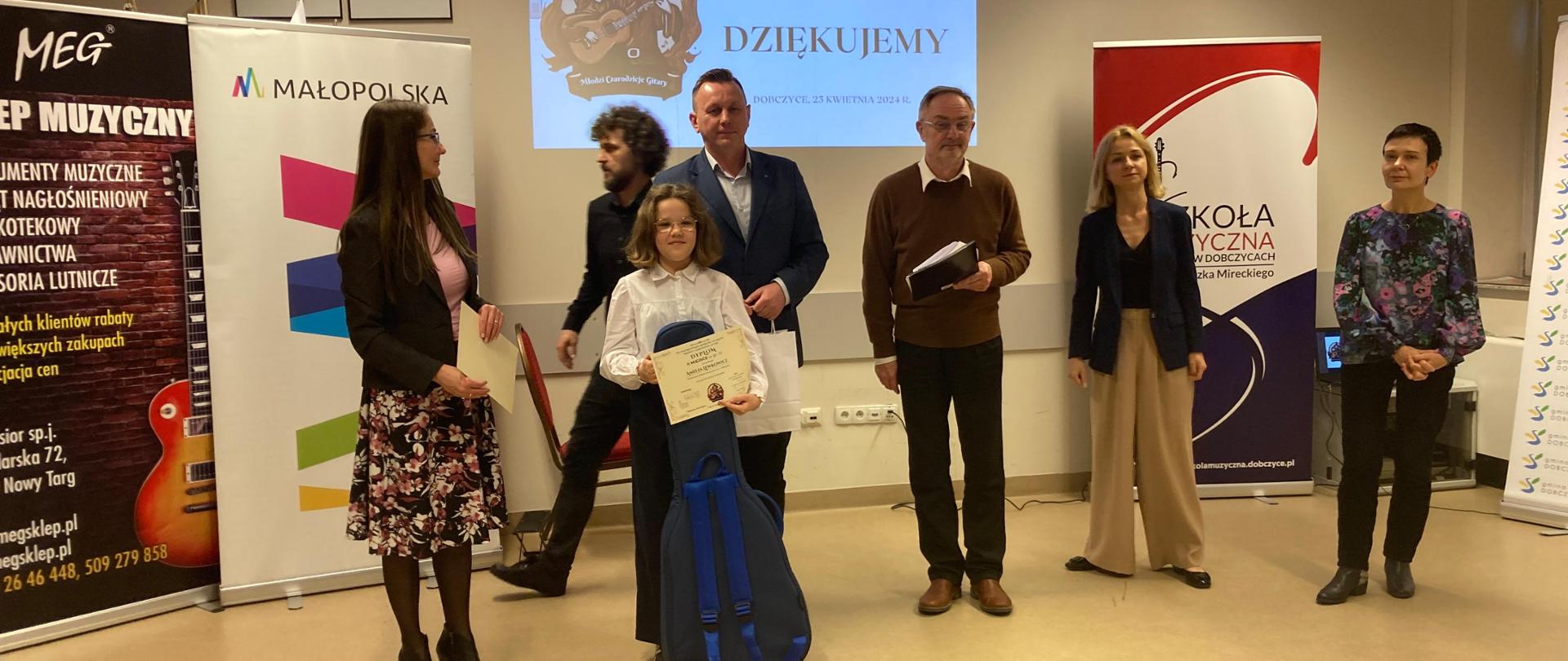 W dniu 25 kwietnia 2024 odbył się VII Ogólnopolski Konkurs Gitarowy "Młodzi czarodzieje gitary" w Dobczycach. Uczennica naszej szkoły Amelia Lewkowicz z klasy IV/6 pani Iwony Grabowskiej zajęła II miejsce w gr. III. Na zdjęciu Amelia stoi wraz z jurorami konkursu, dyrekcją szkoły. Trzyma nagrodę - pokrowiec gitarowy i dyplom.