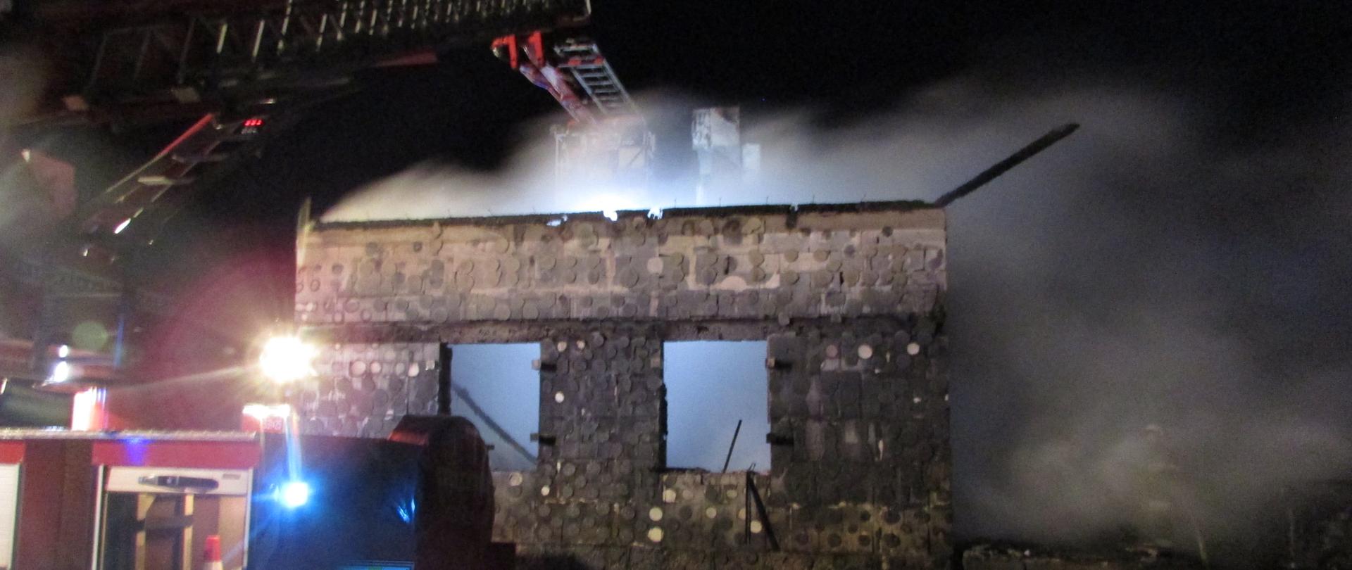 Ściana budynku po pożarze w nocy. Widoczny dym i samochód pożarniczy drabina.