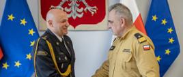 Na zdjęciu widoczni na tle orła białego i flag biało czerwonej i unijnej z-ca komendanta głównego nadbryg.Józef Galica wręczający akt powołania na stanowisko zastępcy małopolskiego komendanta wojewódzkiego PSP st. bryg. dr inż. Arkadiuszowi Kielin.