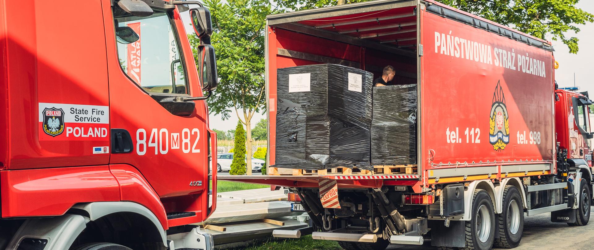 Zdjęcie przedstawia załadunek wozów strażackich.