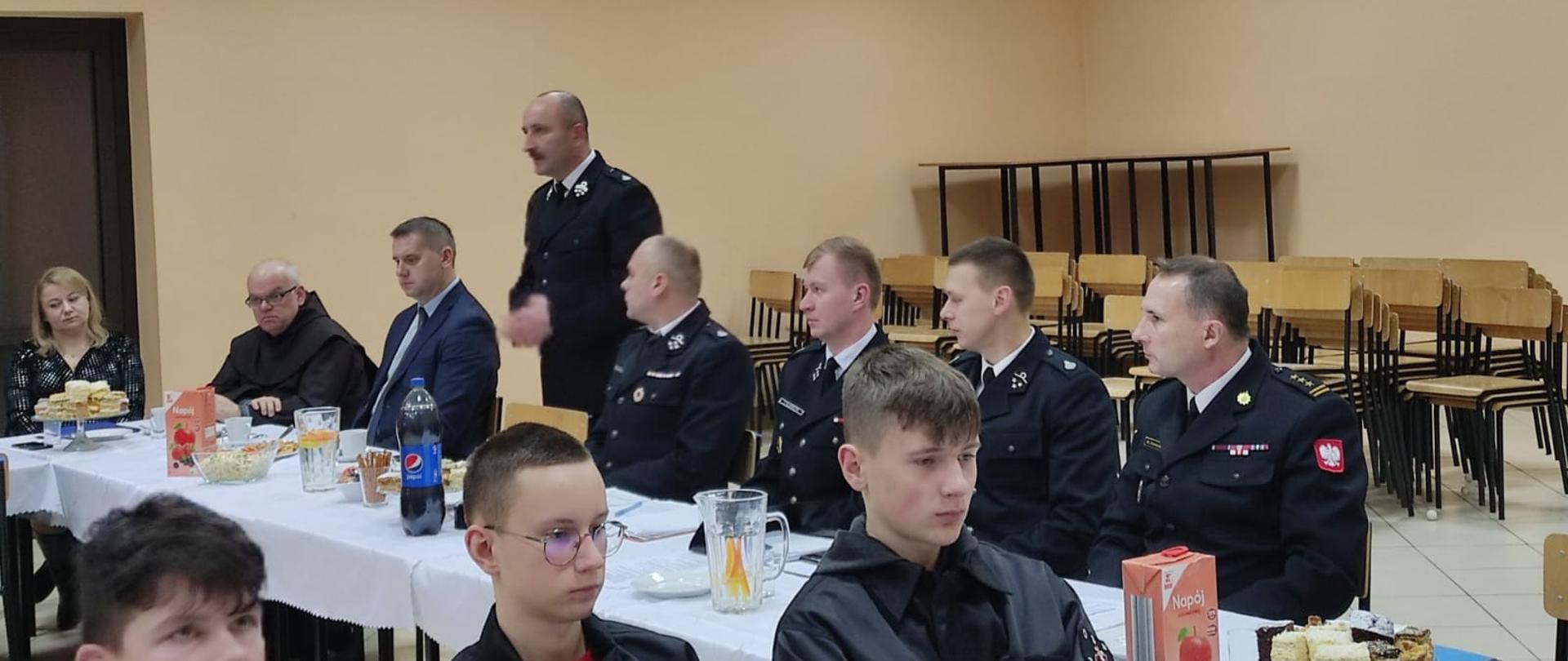 Zdjęcie przedstawia druhów oraz zaproszonych gości podczas spotkania noworocznego. Głos zabiera pan Mariusz Ściana członek zarządu Starostwa Powiatowego w Kielcach.