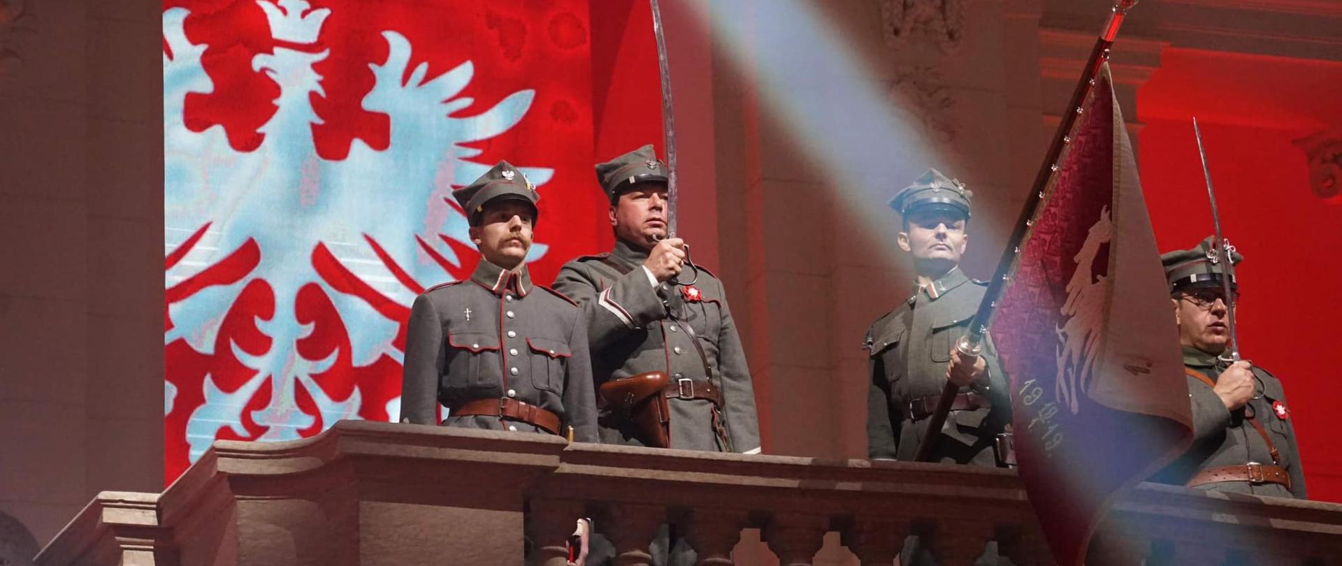 widowisko, żołnierze stoją na balkonie, w tle na czerwonym materiale biały orzeł