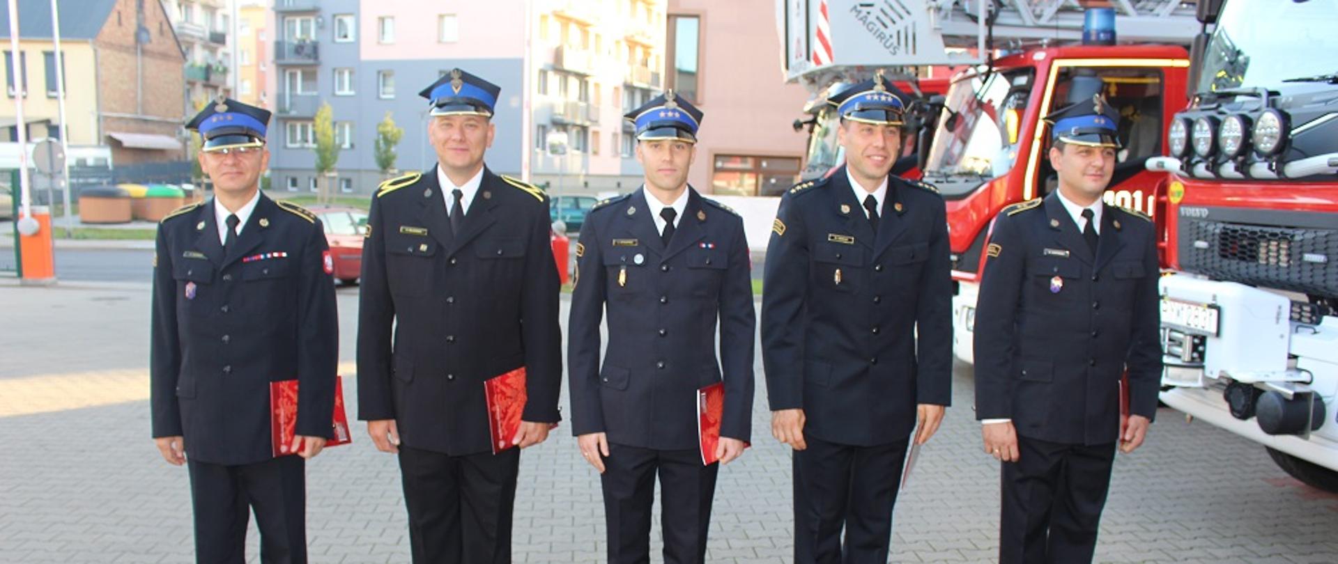 Zdjęcie przedstawia strażaków podczas uroczystej zmiany służby.
W tle plac JRG i samochody strażackie.
