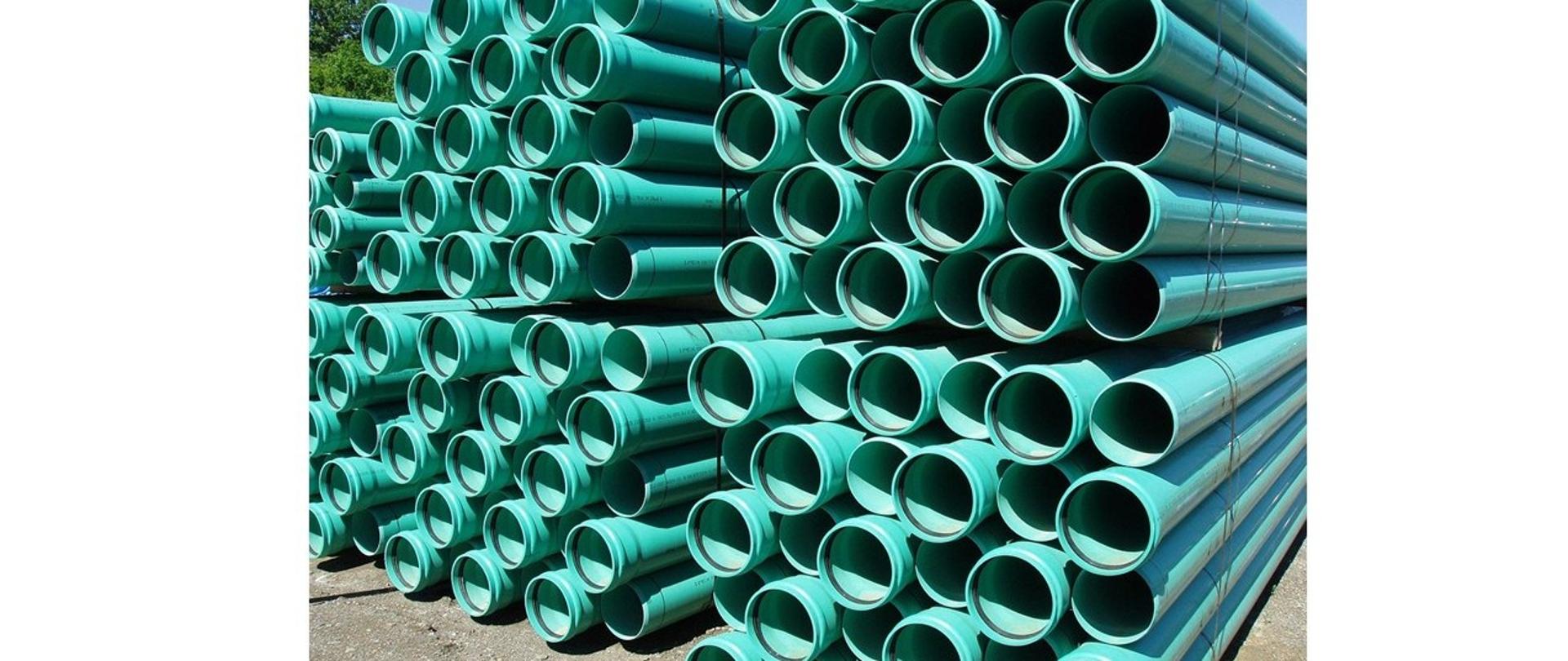 Na zdjęciu zielone rury kanalizacyjne składowane jedna na drugiej
