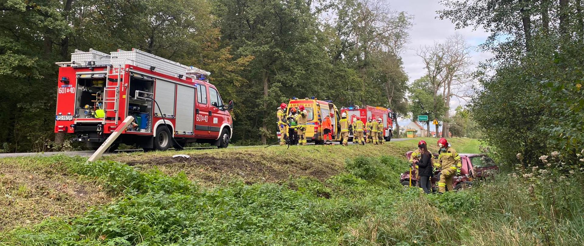 Na zdjęciu pojazdy pożarnicze z ratownikami oraz pojazd osobowy biorący udział w zdarzeniu w rowie