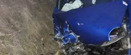 Samochód osobowy koloru niebieskiego znajduje się w rowie z mocno rozbitym przodem samochodu. 