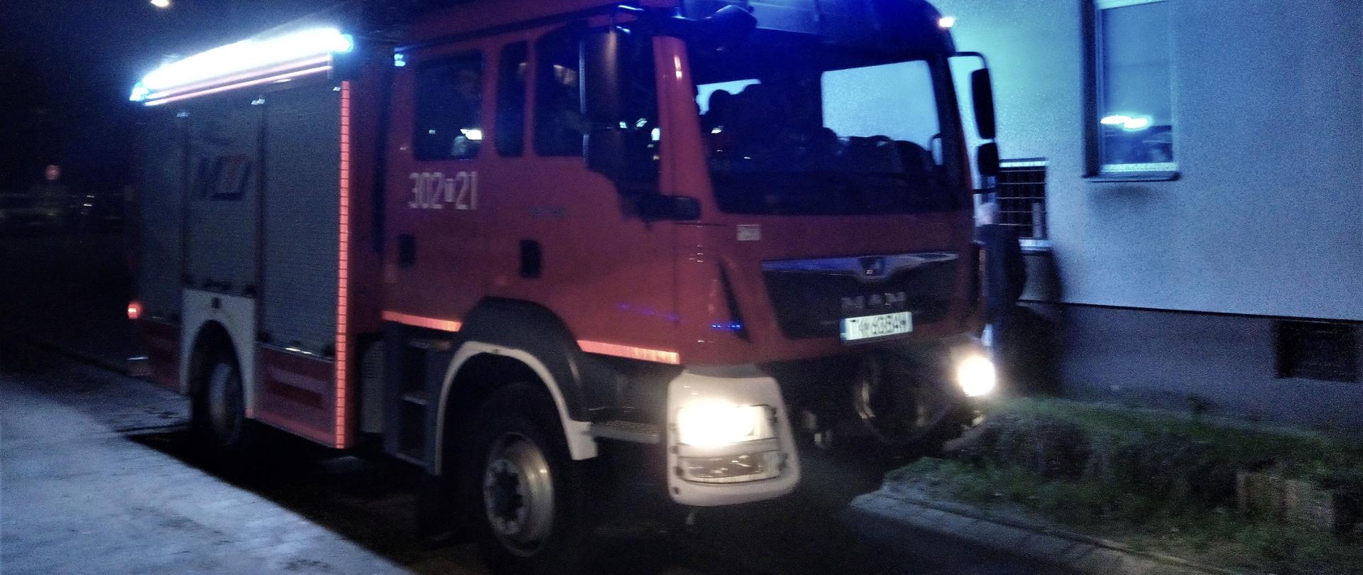 Zdjęcie przedstawia samochód pożarniczy stojący pod budynkiem gdzie doszło do zapalenia się rozdzielni elektrycznej. 