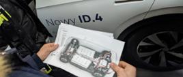 Strażacy oglądają pojazd elektryczny VW ID. 4 pod kątem występowania zagrożeń podczas jego pożaru. Przedstawiciel; dealera prezentuje schematy elektryczne.