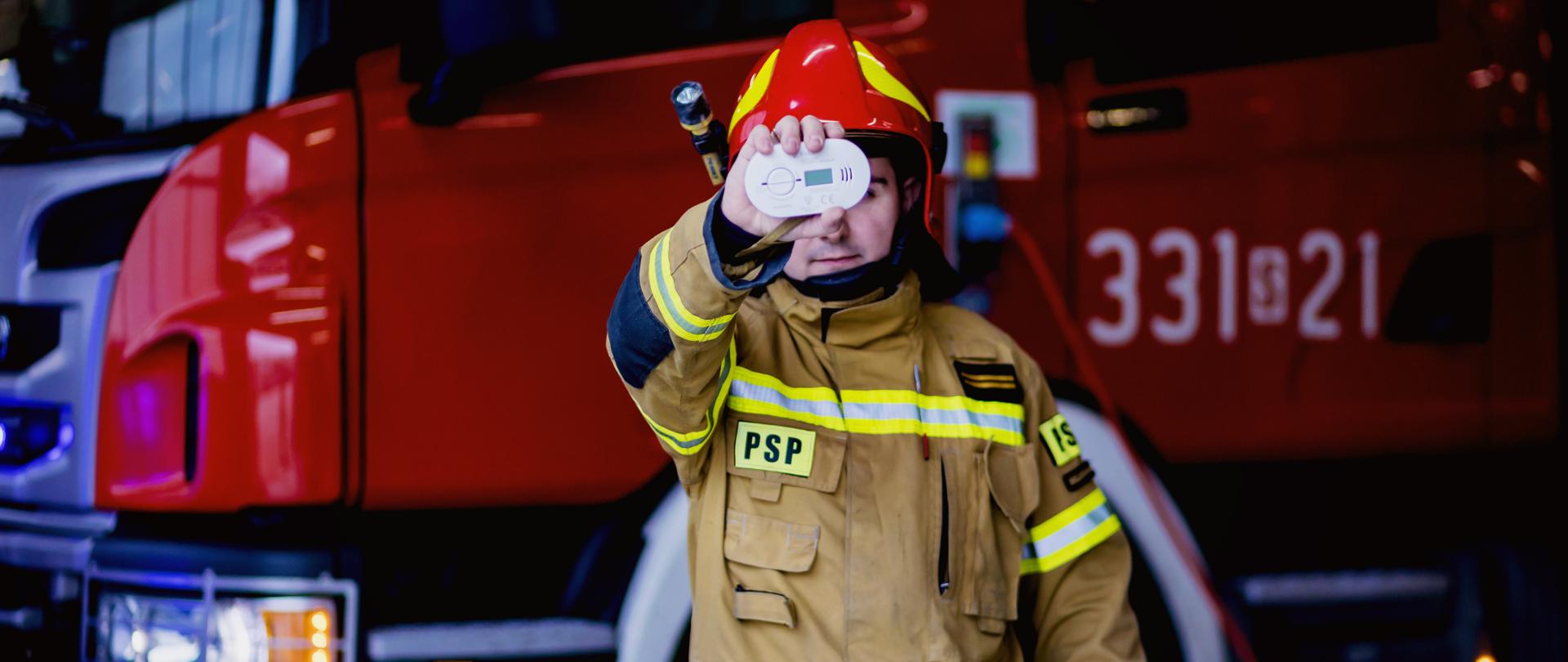Strażak trzymający czujnik czadu na tle samochodu pożarniczego
