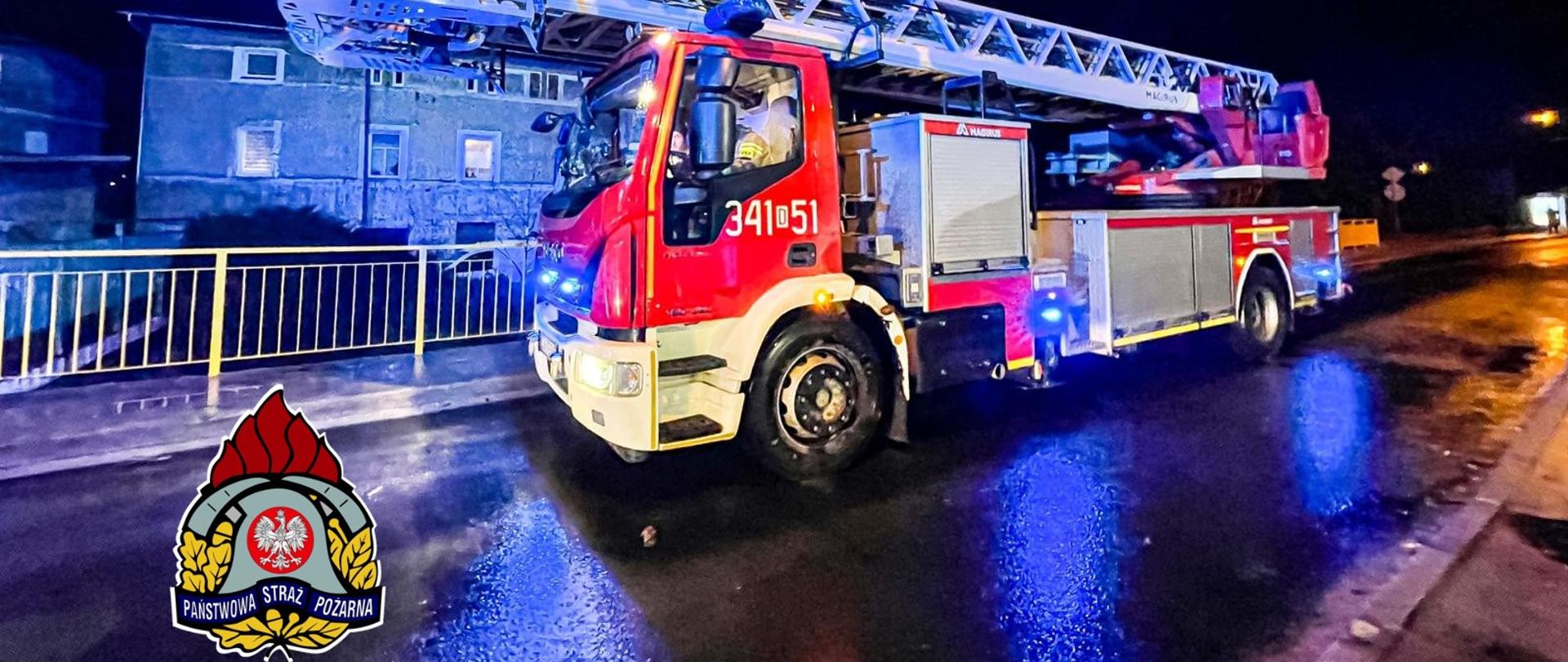 Na zdjęciu widać samochód drabina SCD 42 znajdujący się na drodze obok budynku. Zdjęcie wykonane w nocy podczas działań. 