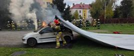 Strażacy z krotoszyńskiej jednostki prowadzą szkolenie z zakresu pożarów samochodów elektrycznych. Uczestnikami są strażacy z jednostek OSP. Strażacy demonstrują gaszenie pożaru z użyciem płachty gaśniczej, pracując w sprzęcie ochrony dróg oddechowych. 