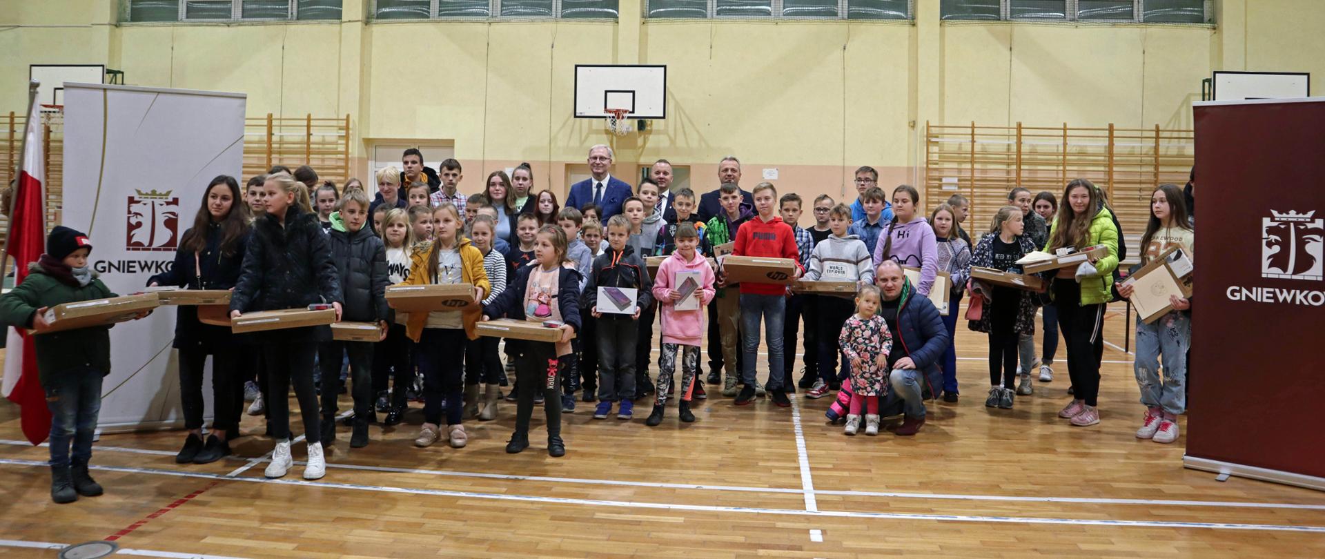 Zdjęcie zbiorowe - na pierwszym planie dzieci i młodzież, które otrzymały sprzęt komputerowy. 