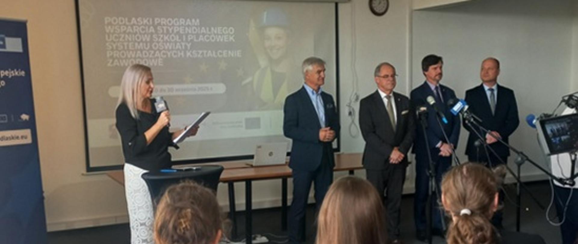 Grupa osób stojących przy mikrofonach przed słuchaczami