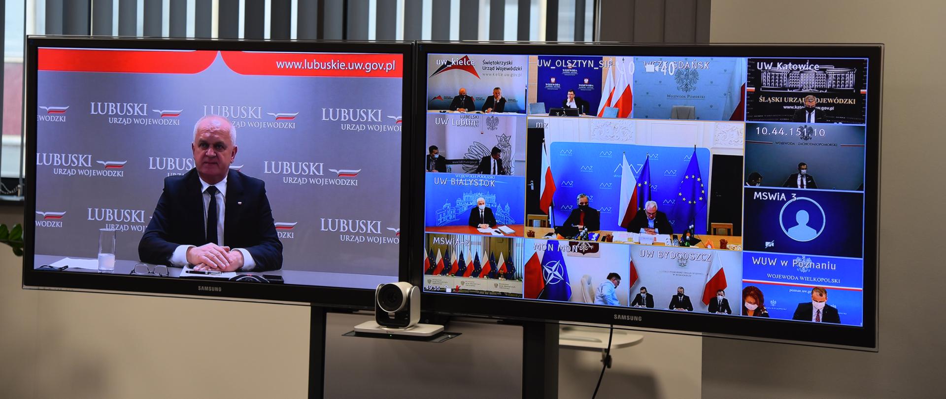 Dwa ekrany stoją na tle okna z lekko otwartymi żaluzjami. Na lewym ekranie wojewoda na tle ścianki promocyjnej Lubuskiego Urzędu wojewódzkiego. Na prawym ekranie 13 miniatur z przedstawicielami ministerstw i innych województw 
