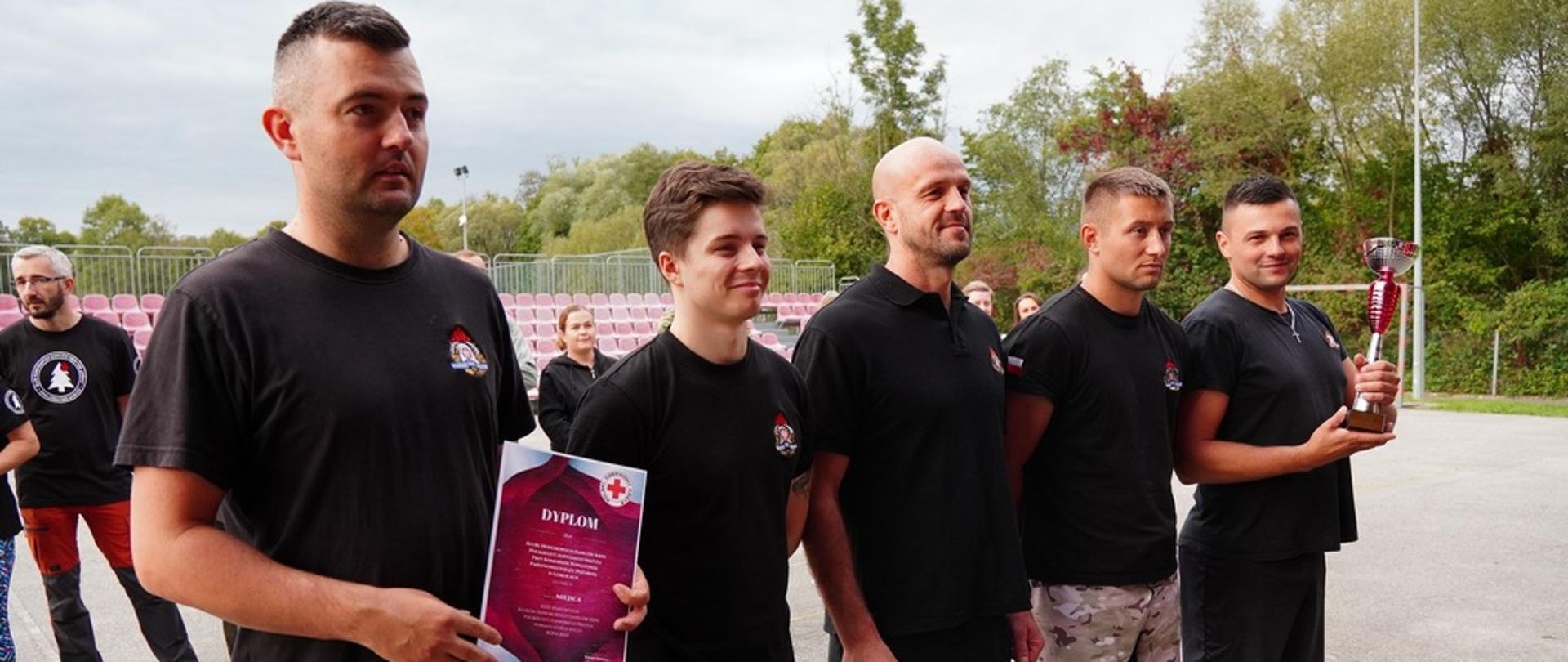 Na zdjęciu widoczna drużyna stojąca w jednym szeregu biorące udział w XXXI Spartakiadzie Honorowych Dawców Krwi Polskiego Czerwonego Krzyża w Ropie podczas wręczania pucharu i dyplomu za pierwsze miejsce.