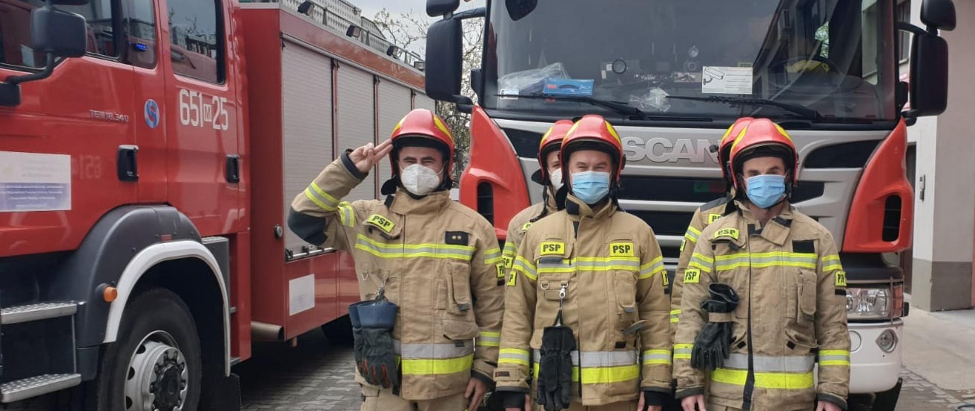 Fotografia przedstawiająca strażaków na baczność na tle pojazdów bojowych oddających hołd poległemu na służbie policjantowi asp. Michałowi Kędzierskiemu.