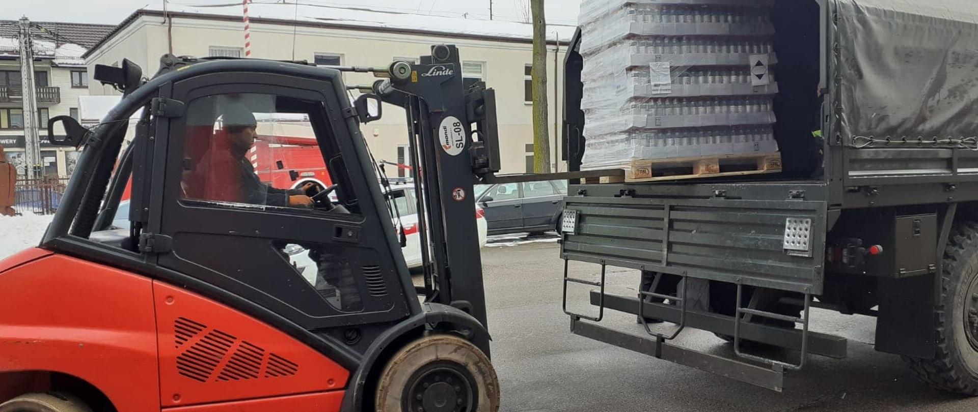Strażak rozładowuje paletę z płynem do dezynfekcji przy pomocy wózka widłowego z wojskowego samochodu ciężarowego.