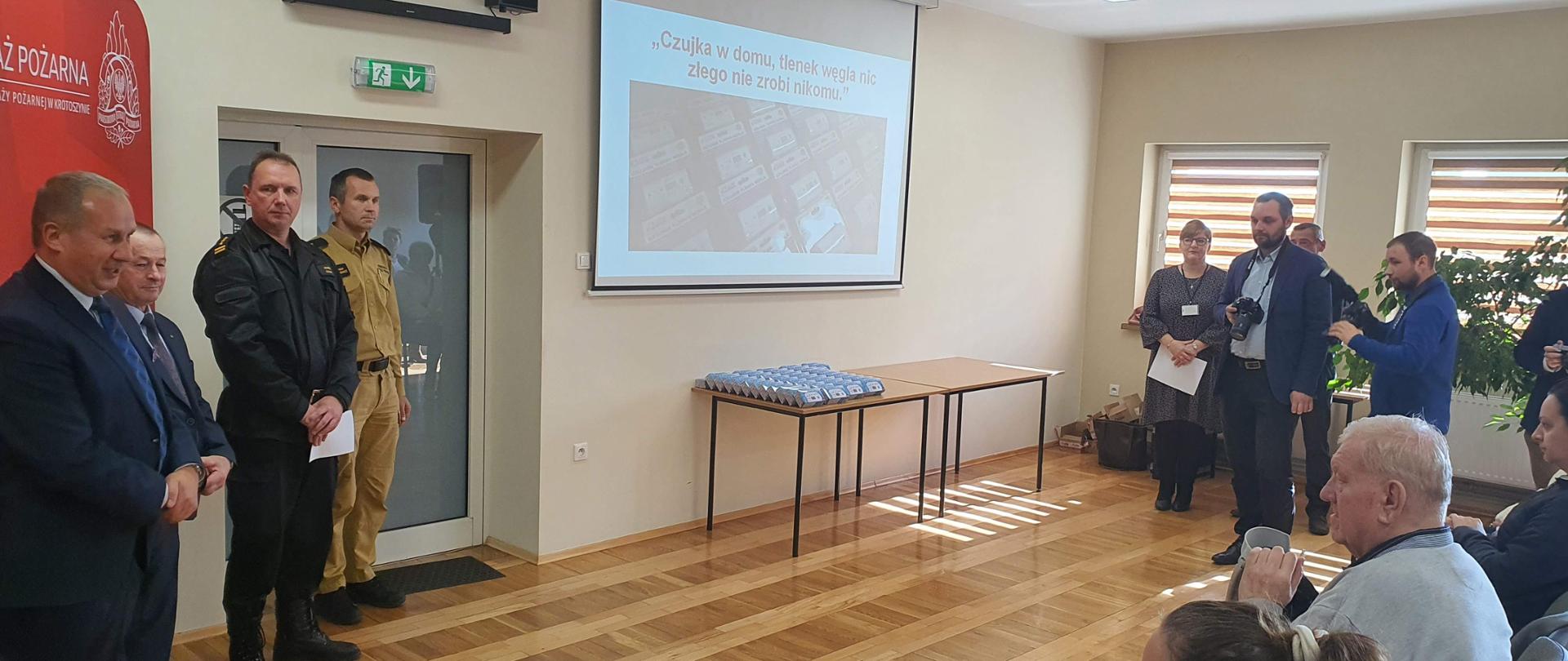 Na świetlicy komendy powiatowej PSP w Krotoszynie odbyła się uroczystość wręczenia czujników tlenku węgla rozlosowanych w ramach konkursu "Czujka w domu, tlenek węgla nie zrobi nic złego nikomu". Na tle baneru komendy powiatowej obecni na uroczystości gości w osobach: Starosty Powiatowego, Burmistrza Krotoszyna oraz kierownictwa krotoszyńskiej komendy witają mieszkańców powiatu składając gratulacje.