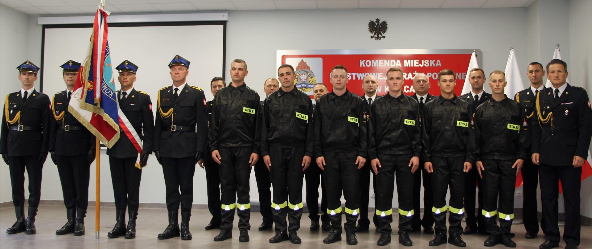 Zdjęcie przedstawia wszystkich uczestników ślubowania. W pierwszym szeregu stoją nowi strażacy, z lewej strony stoi poczet sztandarowy ze sztandarem, a w drugim rzędzie pracownicy Komendy Miejskiej Państwowej Straży Pożarnej w Kielcach wraz z komendantem.