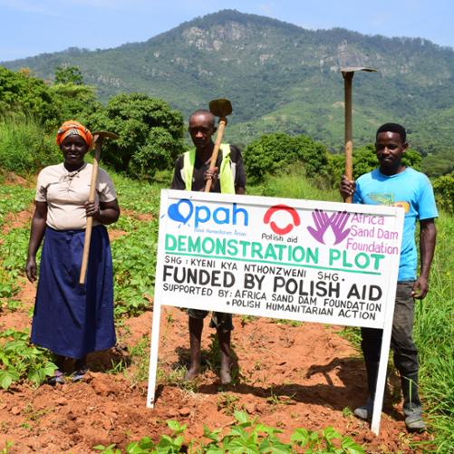 Dwóch mężczyzn i kobieta na modelowym polu uprawnym z tablicą informacyjną