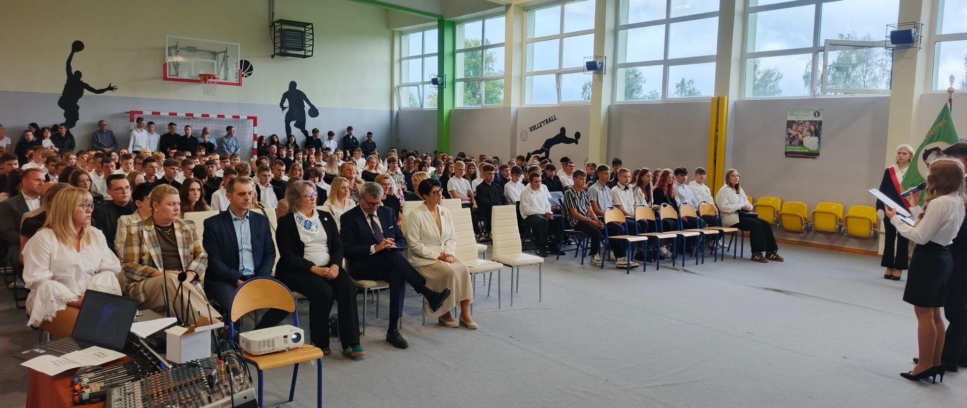 Sala gimnastyczna ZSCKR w Sypniewie, na środku stoją uczniowie prowadzący oraz cała szala siedzących nauczycieli i uczniów.