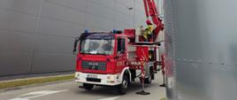 Strażacy w koszu wysięgnika hydraulicznego na wysokości dachu podczas ćwiczeń na obiekcie firmy produkcyjnej