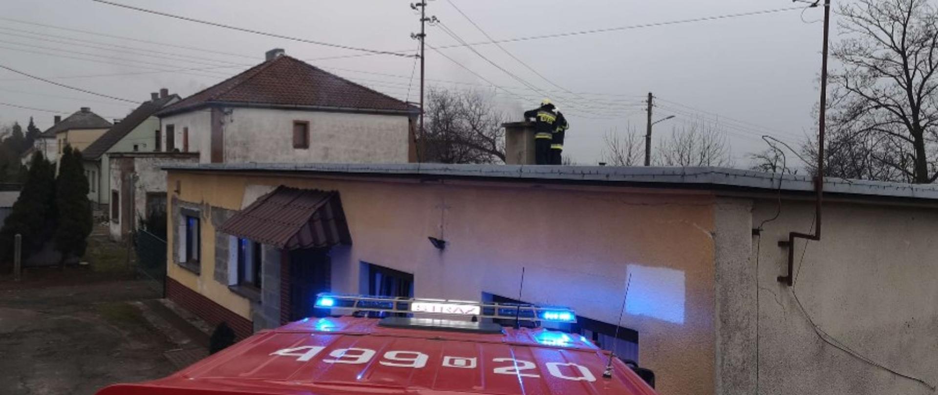 Zdjęcie przedstawia samochód strażacki z perspektywy dachu oraz dwóch strażaków na dachu budynku