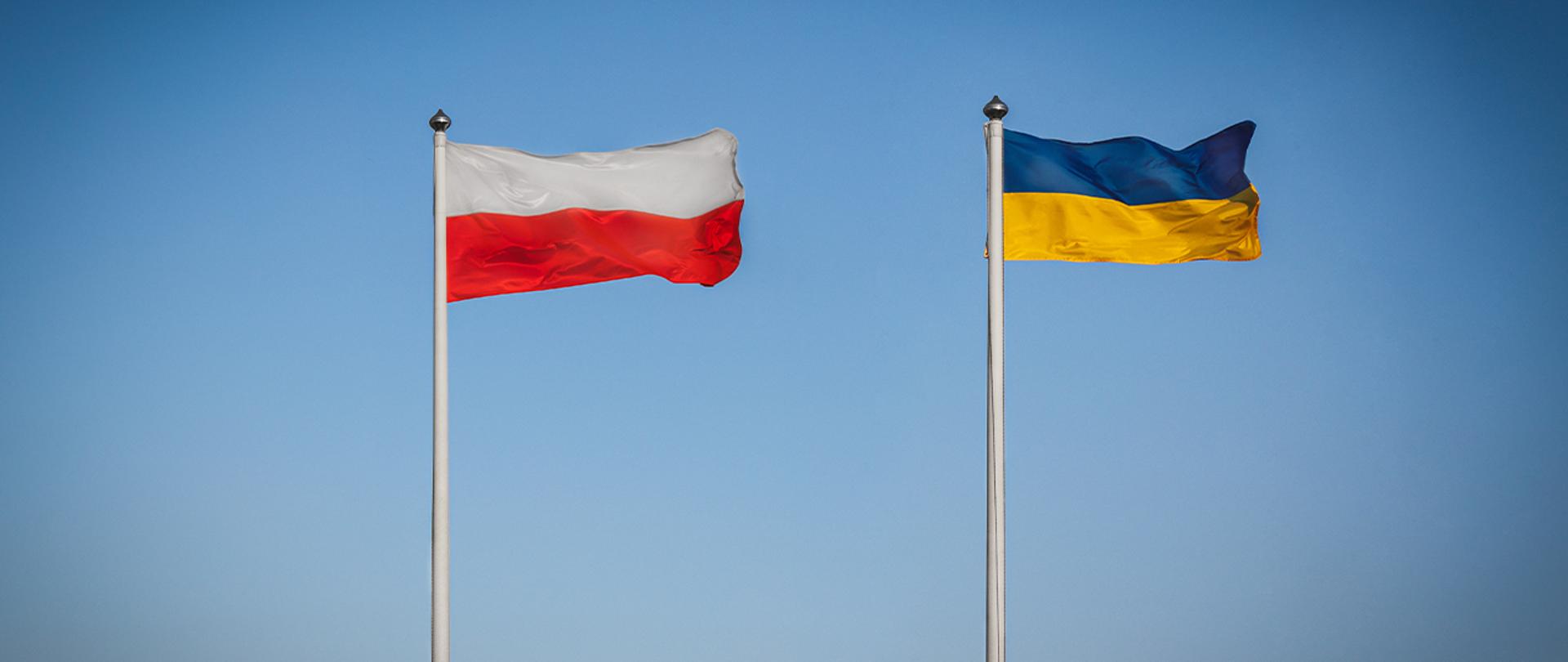 Powiewające flagi: Polski biało-czerwona i Ukrainy niebiesko-żółta na tle błękitnego nieba. 