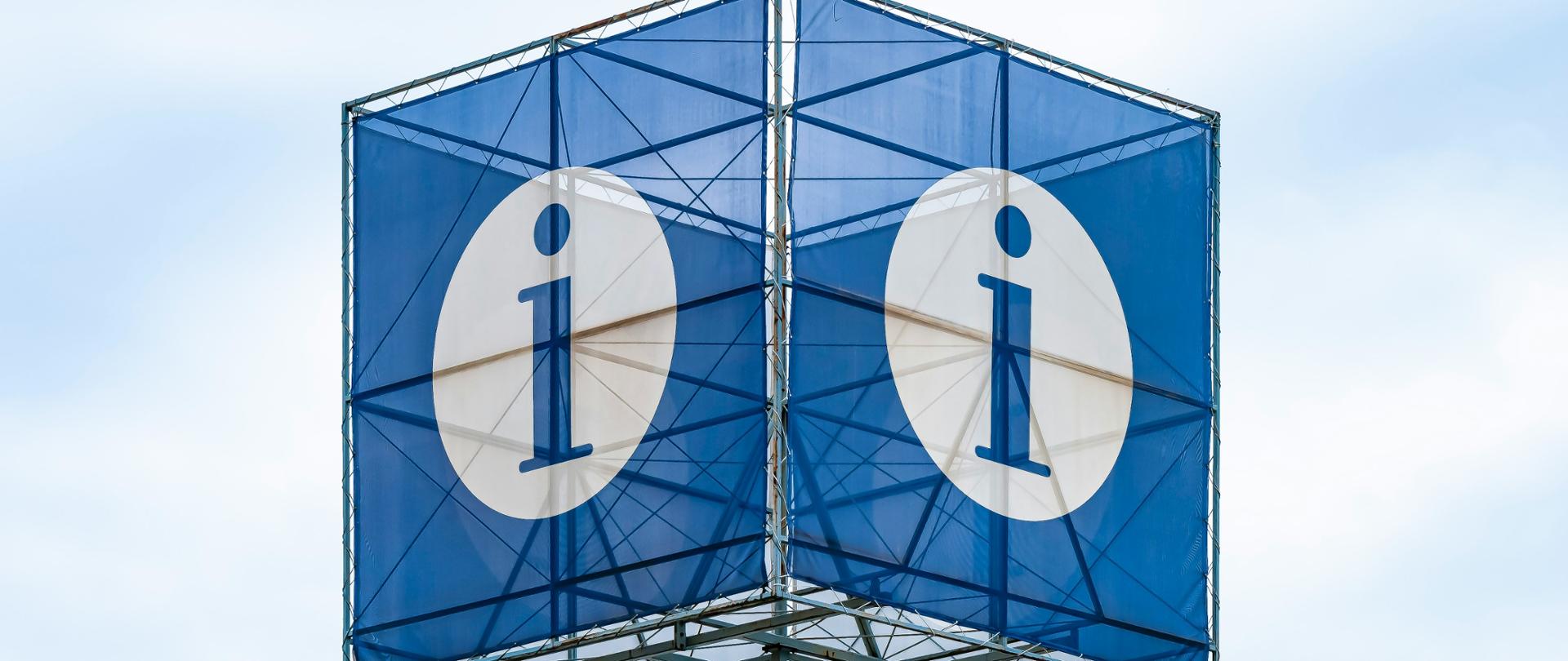 Litera i na granatowym tle na dużym metalowym słupie 