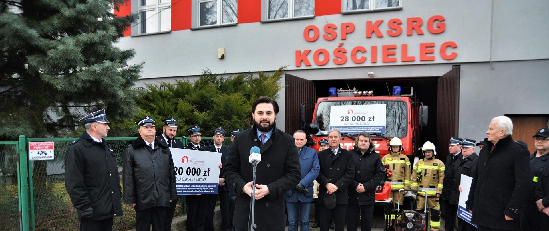 Wiceminister Norbert Kaczmarczyk na uroczystości przekazania środków finansowych dla OSP z powiatu proszowickiego. Wiceminister przemawiający przed remizą strażacką OSP Kościelec. 