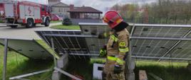 Szkolenie w zakresie bezpieczeństwa działań ratowniczo-gaśniczych podczas zdarzeń z udziałem samochodów elektrycznych i instalacji fotowoltaicznych - na zdjęciu strażak opowiada działanie instalacji fotowoltaicznej, stoi przed taką instalacją.