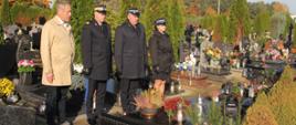 strażacy oraz mężczyzna w jasnym płaszczu stoją przed grobem na cmentarzu