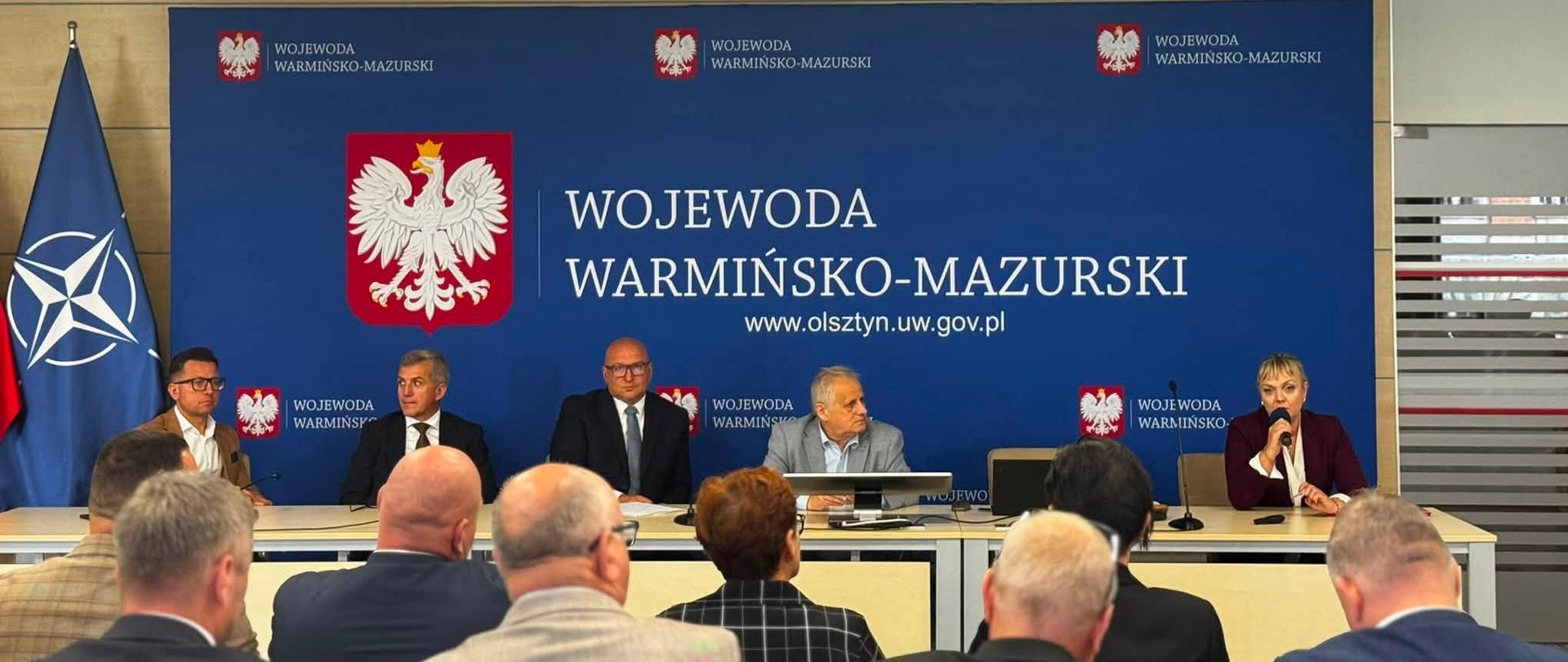 mężczyźni garniturach, w tym wicewojewoda, oraz kobieta w bordowym garniturze siedzą przy stole konferencyjnym 