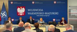 mężczyźni garniturach, w tym wicewojewoda, oraz kobieta w bordowym garniturze siedzą przy stole konferencyjnym 