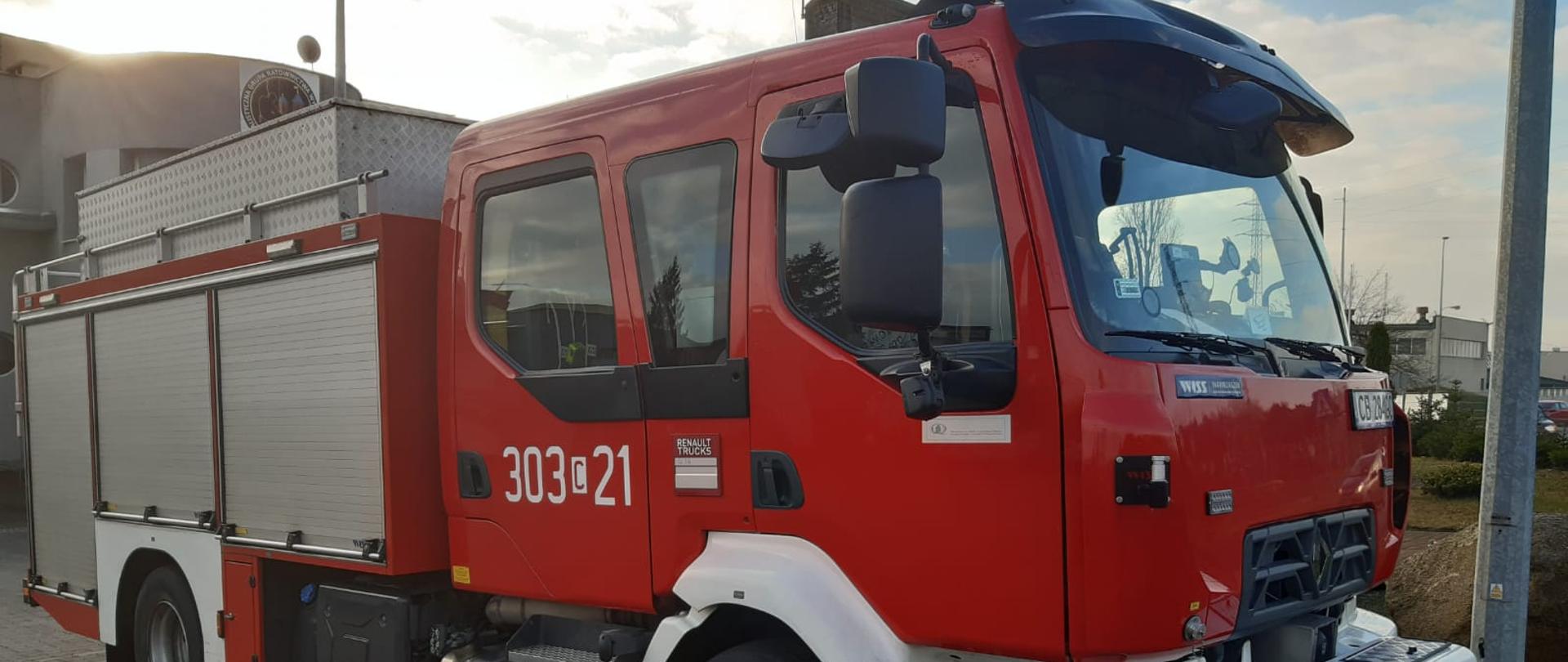 Samochód strażacki ciężarowy ratowniczo-gaśniczy Jednostki Ratowniczo-Gaśniczej nr 3 w Bydgoszczy, podwozie marki Renault, w tle budynek jednostki.