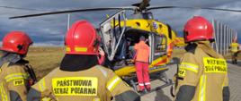 Śmigłowiec na lądowisku oraz strażacy.