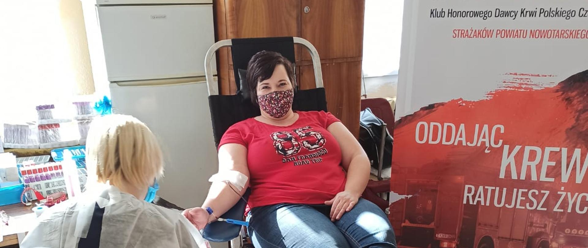 Kobieta na fotelu medycznym do poboru krwi. Baner klubu Nowotarska Strażacka Kropla HDK PCK Strażaków Powiatu Nowotarskiego nr 408. Urządzenie do pobierania krwi, lodówka, pielęgniarka, wiaderko na odpady medyczne.