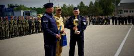 Kierownictwo Policji oraz Państwowej Straży Pożarnej stoi z nagrodami i pucharami, za nimi stoją ustawieni uczniowie klas mundurowych.