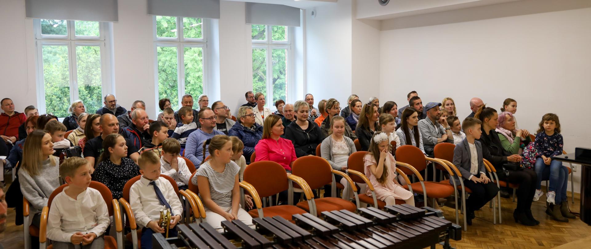 Koncerty uczniów klasy pierwszej. Zdjęcie przedstawiające widok publiczności zgromadzonej na koncercie uczniów klas pierwszych. Zdjęcie wykonane ze sceny. Na pierwszym planie widoczny stojący na scenie ksylofon.