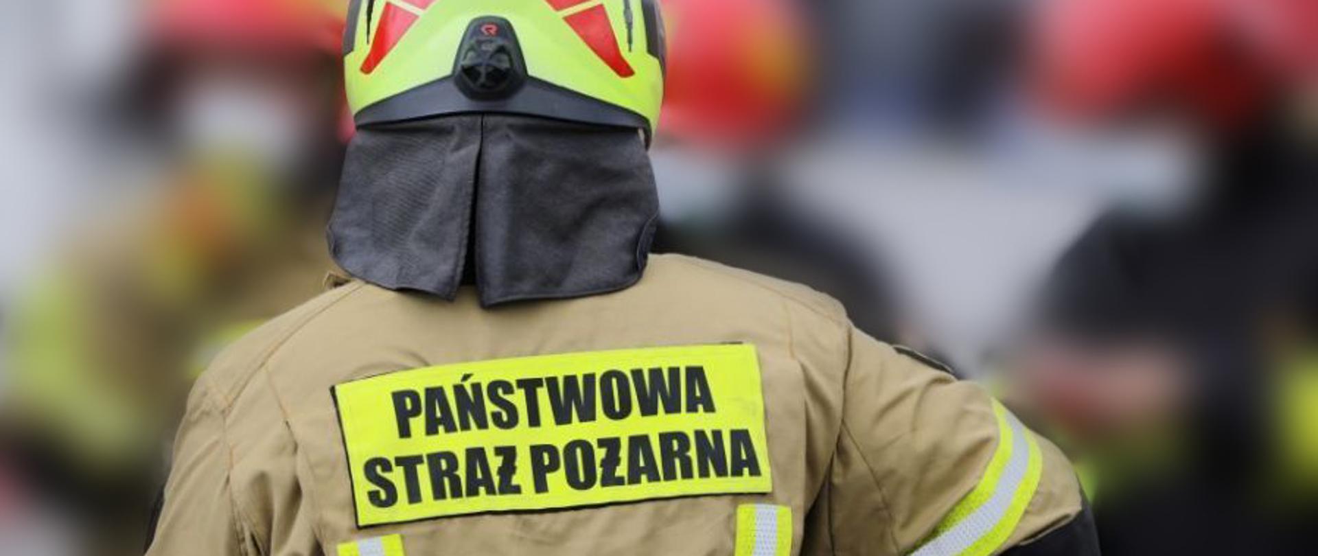Odwrócony tyłem strażak w hełmie z napisem na plecach Państwowa Straż Pożarna