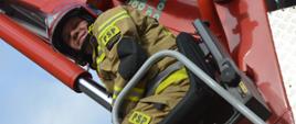 Ćwiczenia w ZOL. Zdjęcie przedstawia strażaka operującego podnosnikiem hydraulicznym. Ma na sobie ubranie specjalne koloru piaskowego i czerwony hełm. Siedzi w fotelu operatora. 