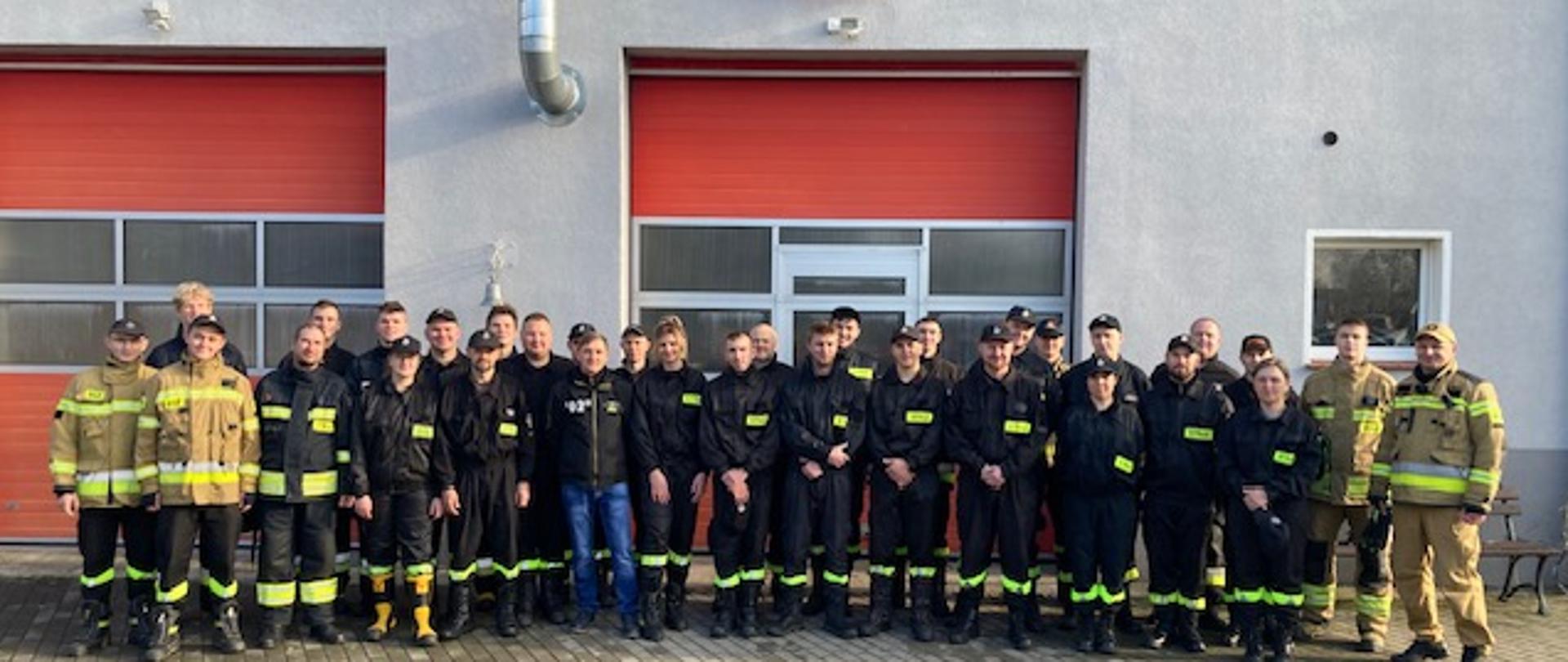 Zbiorowe zdjęcie kilkudziesięciu strażaków Ochotniczej straży pożarnej w mundurach koszarowych wraz z instruktorami pozują do zdjęcia na tle budynku Państwowej straży pożarnej w Sępólnie Krajeńskim