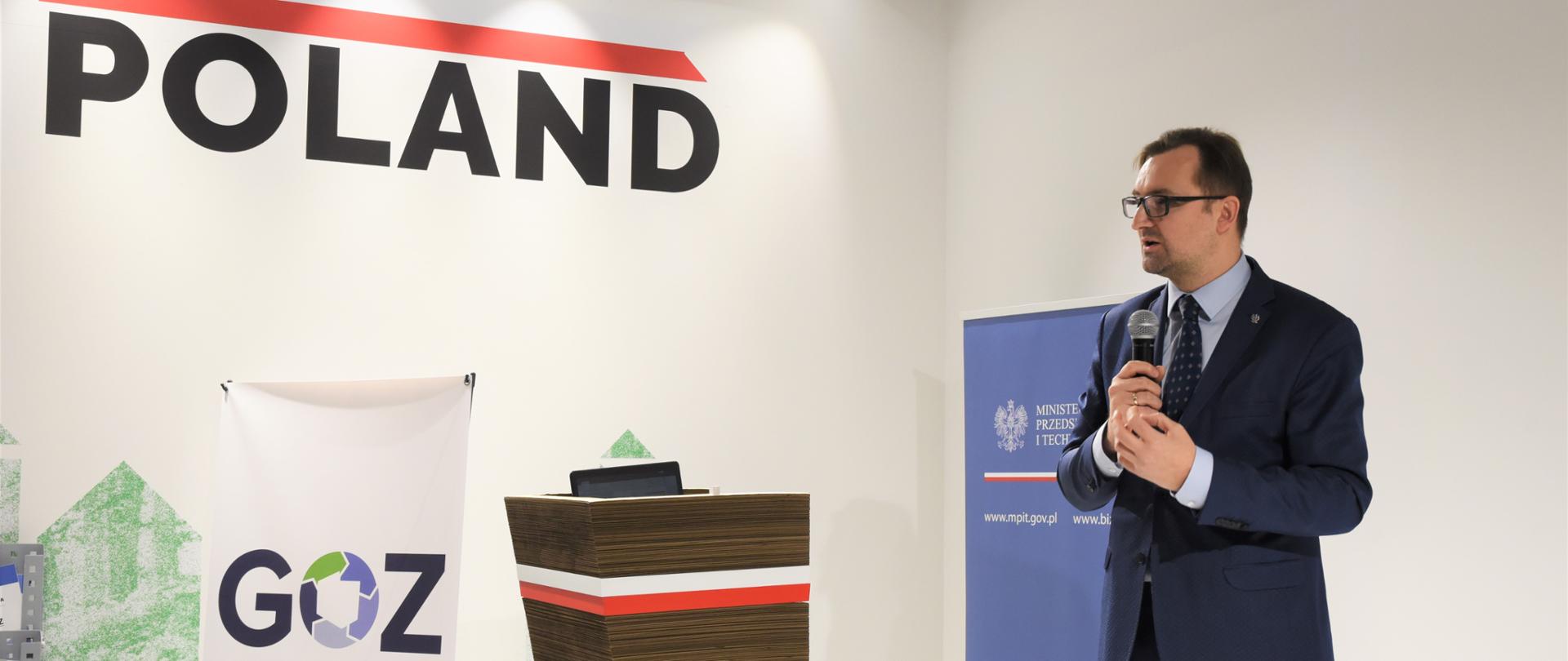 Wiceminister Mazurek, w tle ściana z napisem POLAND.