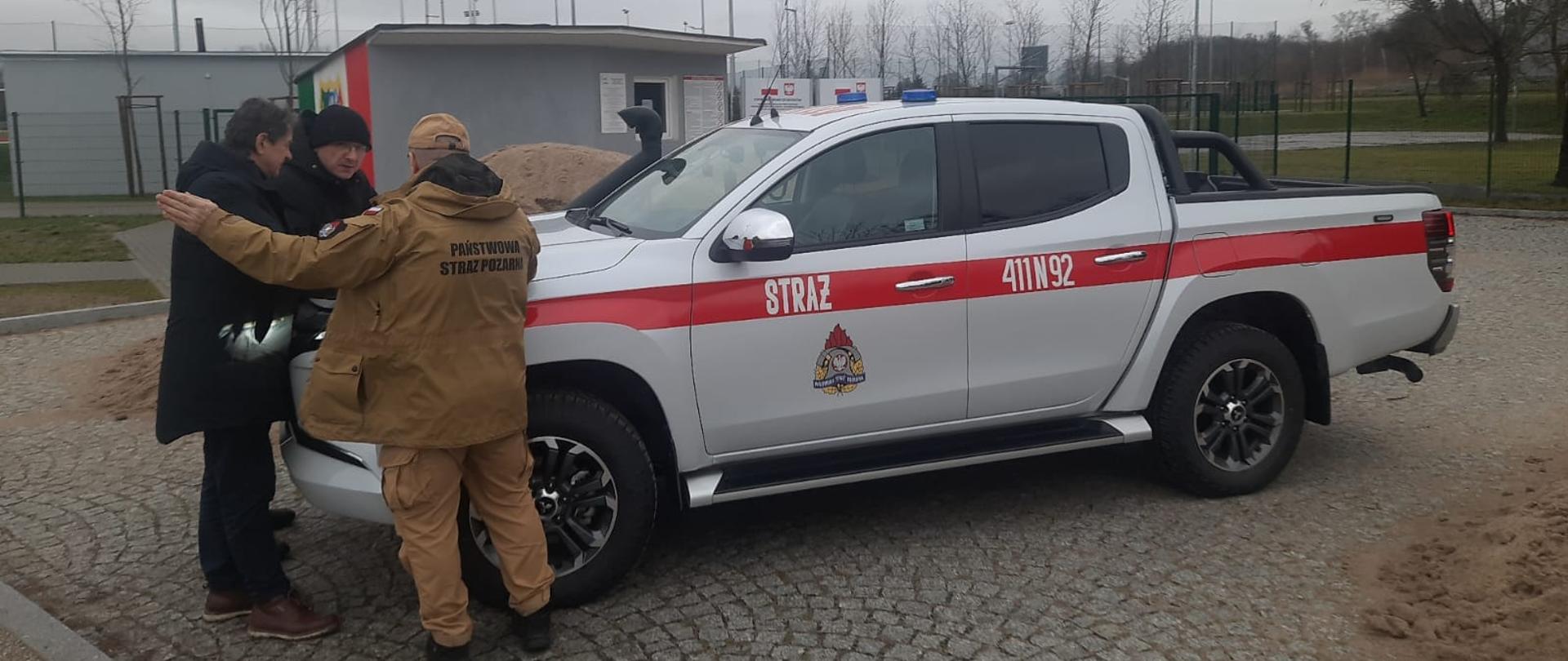 Przy samochodzie strażackim stoi komendant powiatowy, burmistrz Braniewa i starosta braniewski.